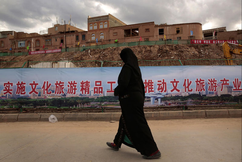 В старых районах Кашгара многие здания выстраиваются заново, некоторые из них были снесены для строительства парка. Женщина проходит мимо строительной площадки.