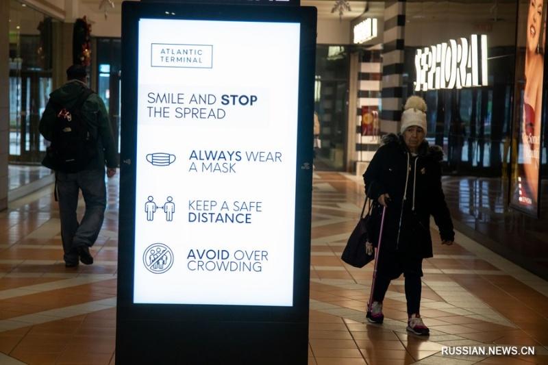 7 декабря 2022 года, Нью-Йорк, США. Люди проходят мимо экрана с рекомендациями носить маски в торговом центре. /Фото Синьхуа/